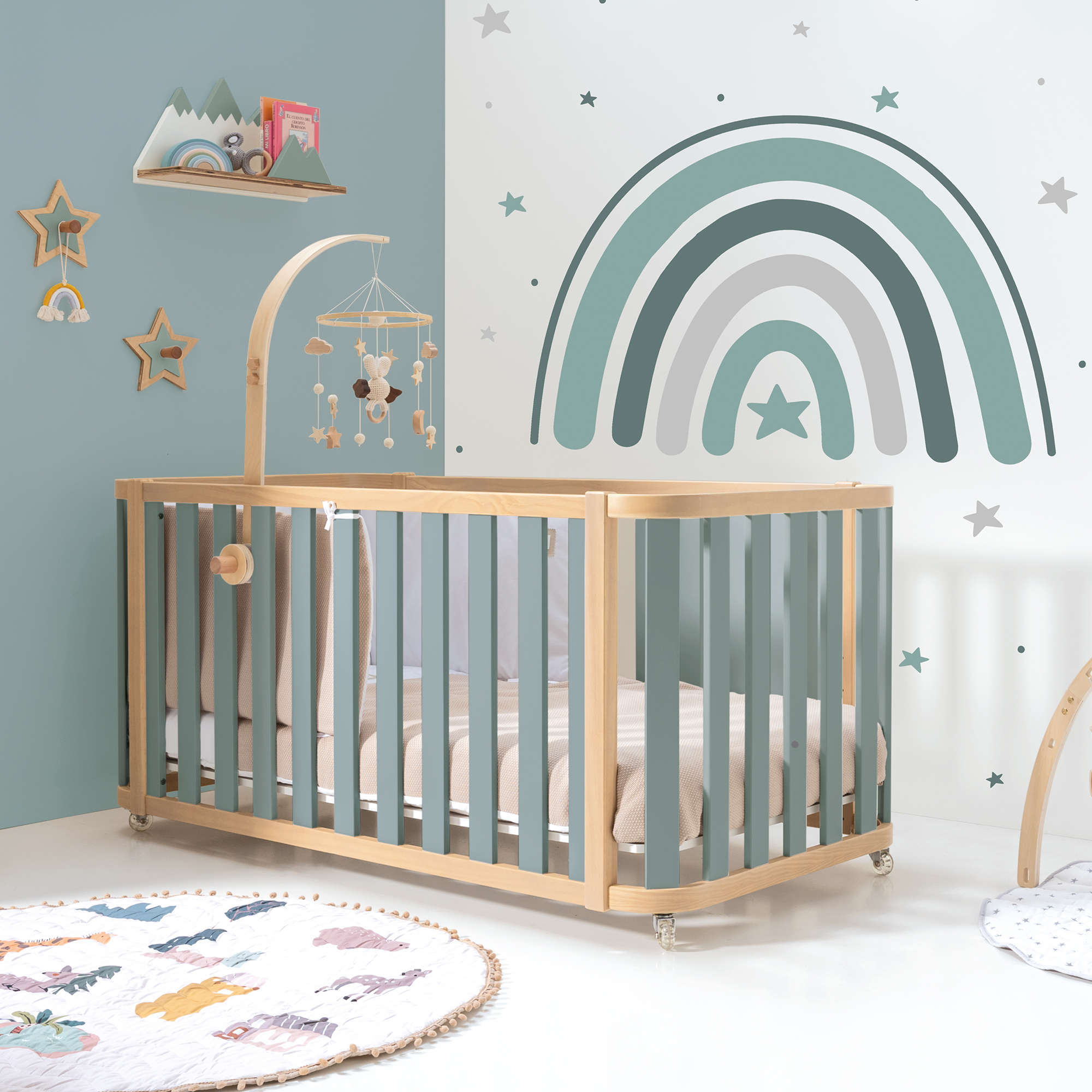 Habitación de bebé con cuna en madera y verde con pared decorada con vinilo de arcoíris
